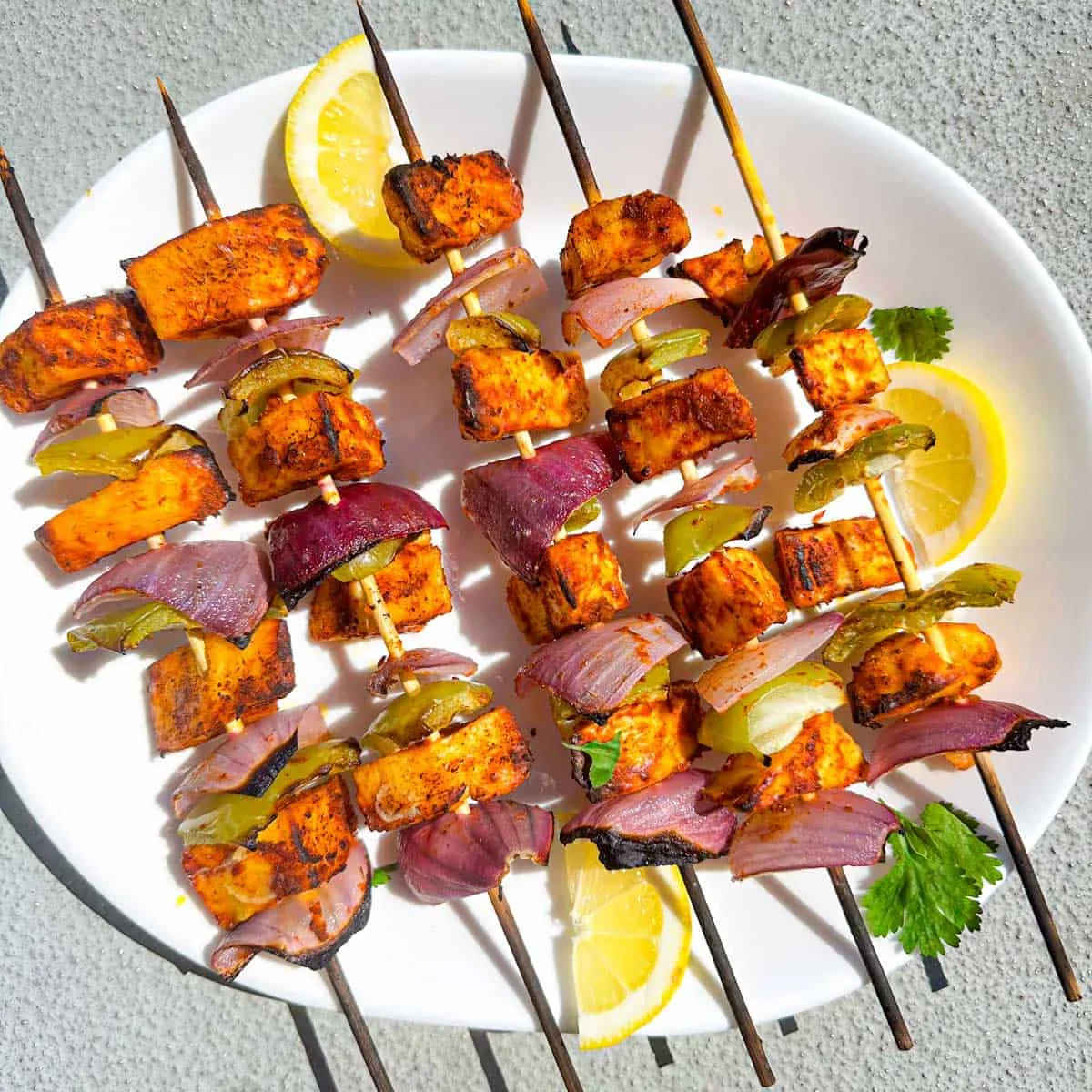 Charred Indian cottage-cheese skewers with fresh lemon on a white platter
